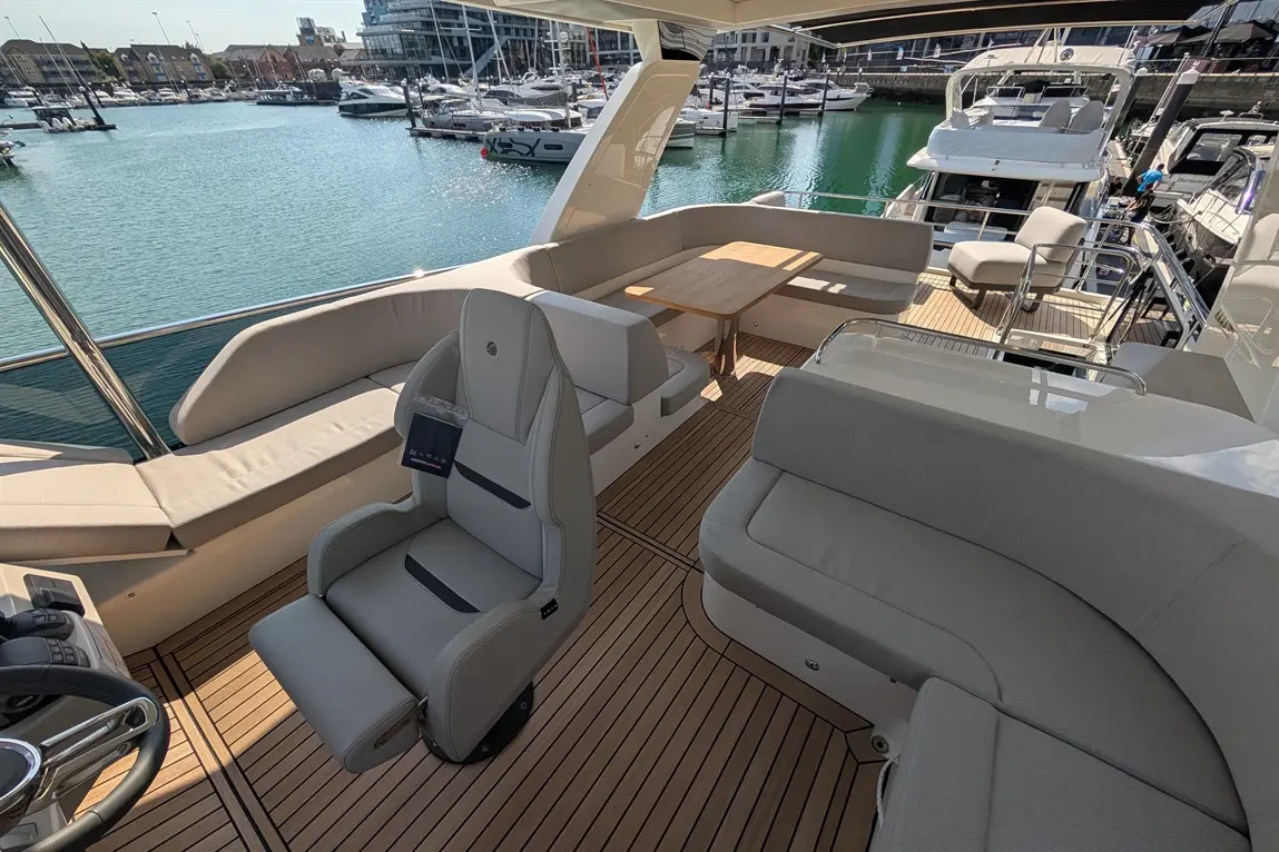 Luxury yacht interior featuring a seating area, wooden deck, and view of marina with moored boats and waterfront buildings.